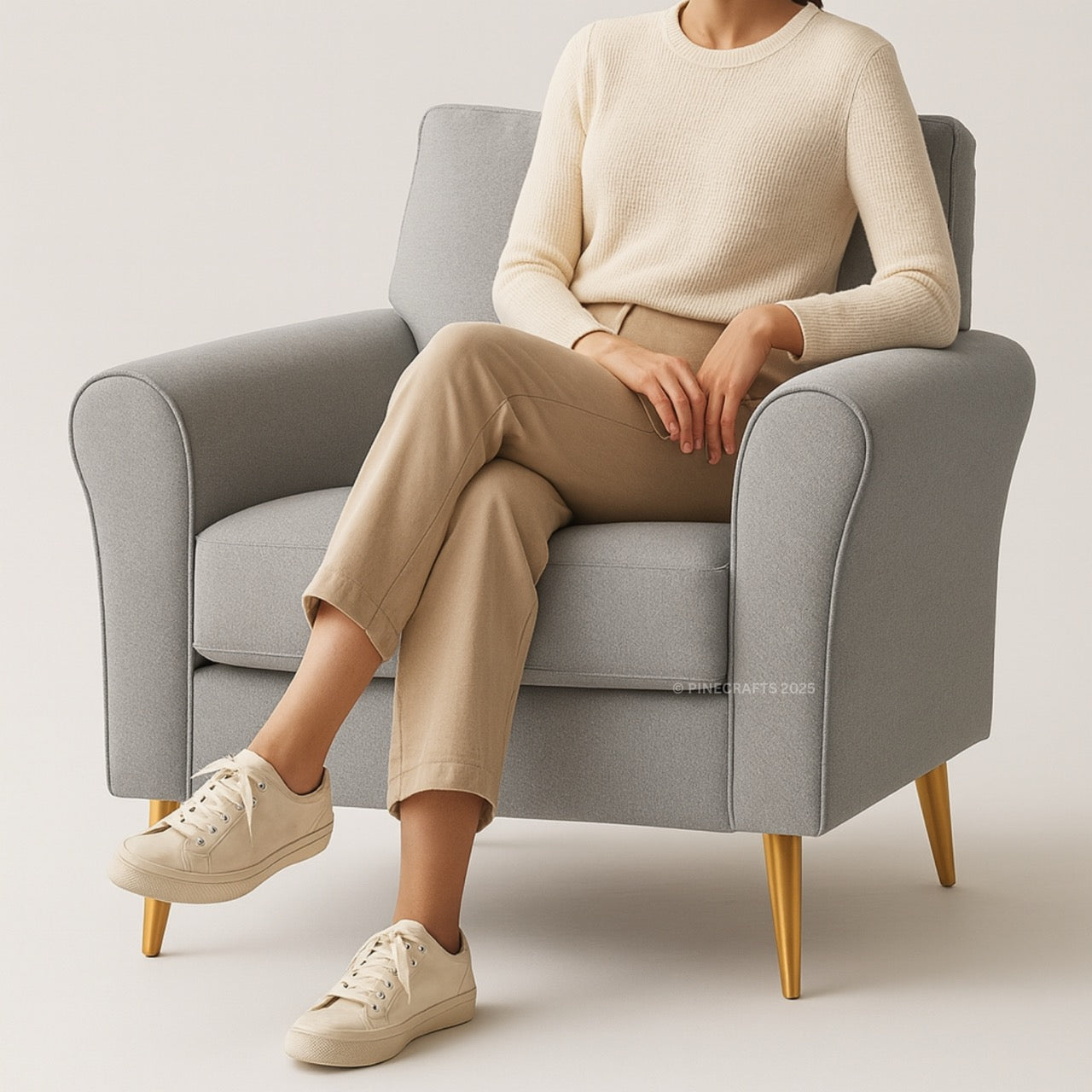 Person sitting on a gray armchair wearing a beige sweater, pants, and shoes.