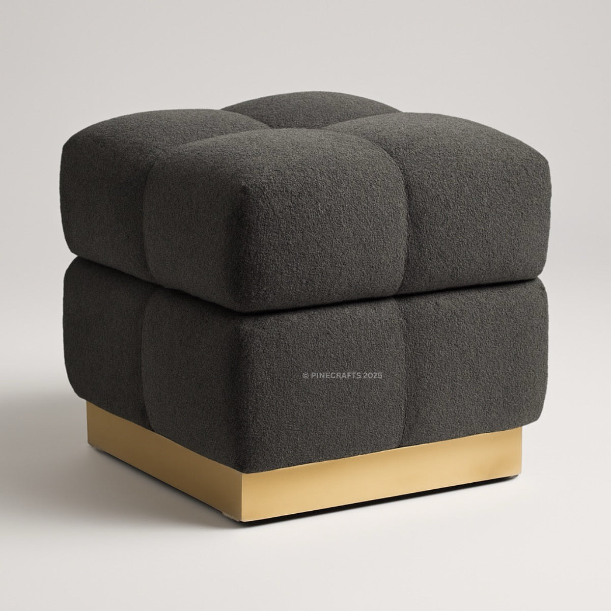 Dark gray upholstered ottoman with a gold base on a light gray background
