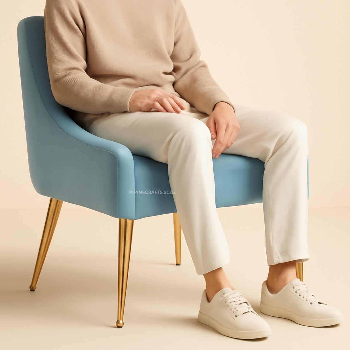 Person sitting on a blue chair wearing a beige sweater, white pants, and white sneakers.