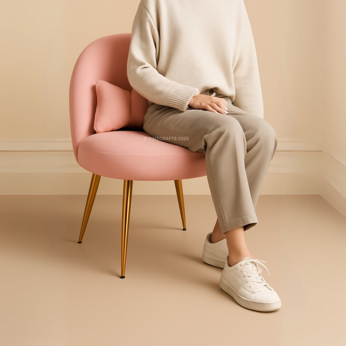Person sitting on a pink chair with gold legs in a minimalistic setting