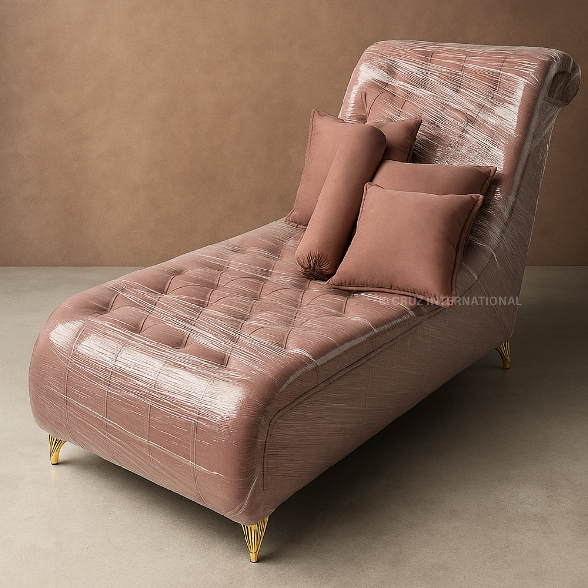 Pink chaise lounge with tufted design and gold legs against a brown wall.