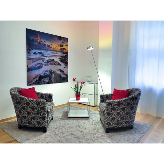 Modern living room with two patterned armchairs, red pillows, glass coffee table, and wall art, showcasing CRUZ INTERNATIONAL furniture style.