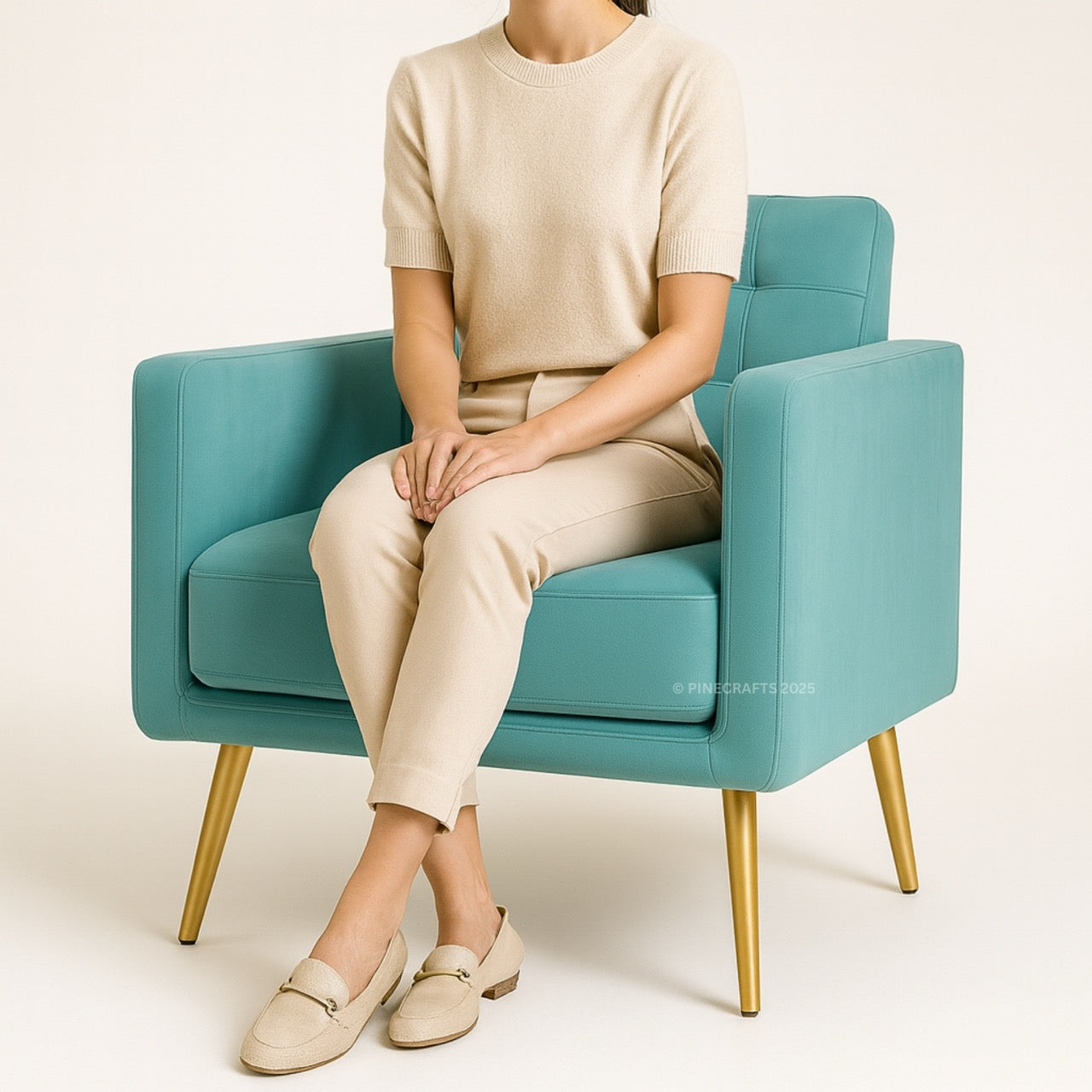 Person sitting on a teal armchair wearing beige clothing against a white background