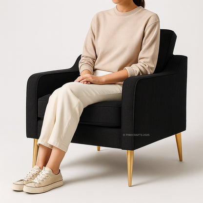 Person sitting on a black armchair wearing a beige sweater and pants with white sneakers.