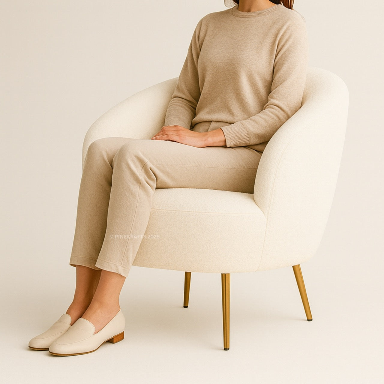 Person wearing a beige sweater and pants sitting on a white chair with gold legs.