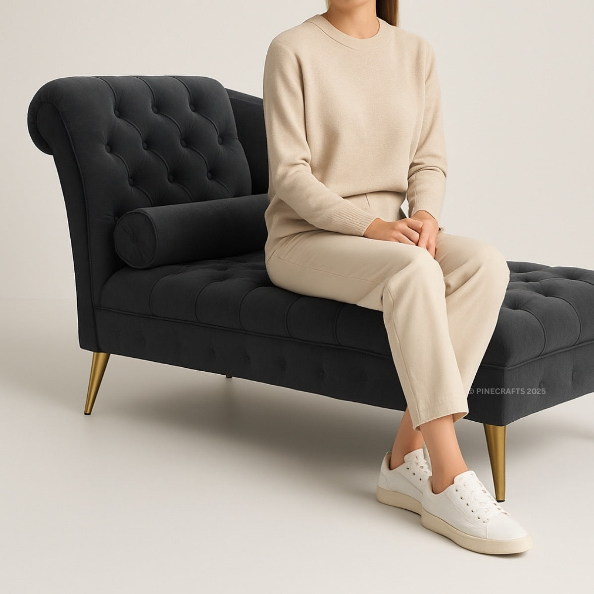 Person sitting on a black tufted sofa wearing a beige outfit and white sneakers.