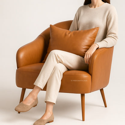 Person sitting on a brown leather armchair with a beige cushion, wearing a beige sweater and pants.