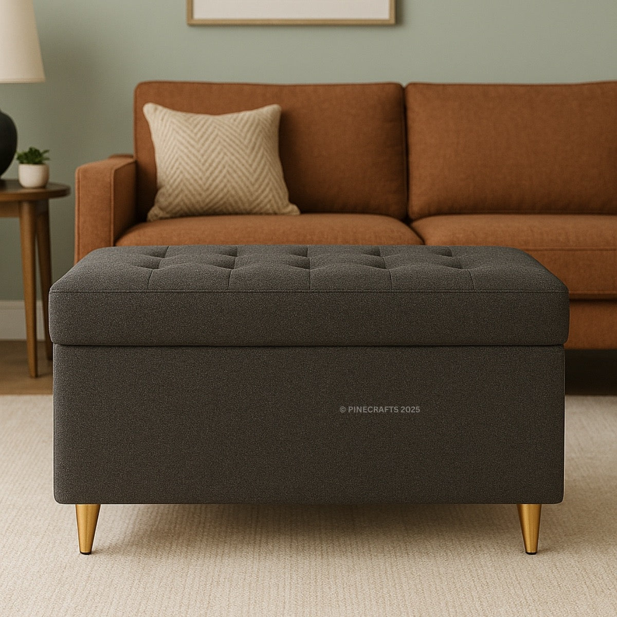 Gray storage ottoman with gold legs in front of a brown sofa in a living room setting.
