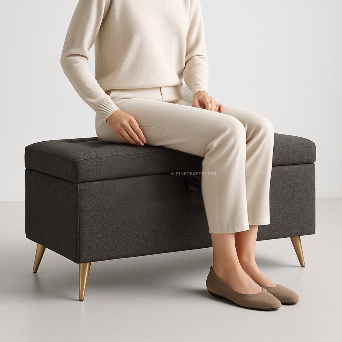 Person sitting on a dark gray storage bench with a plain background