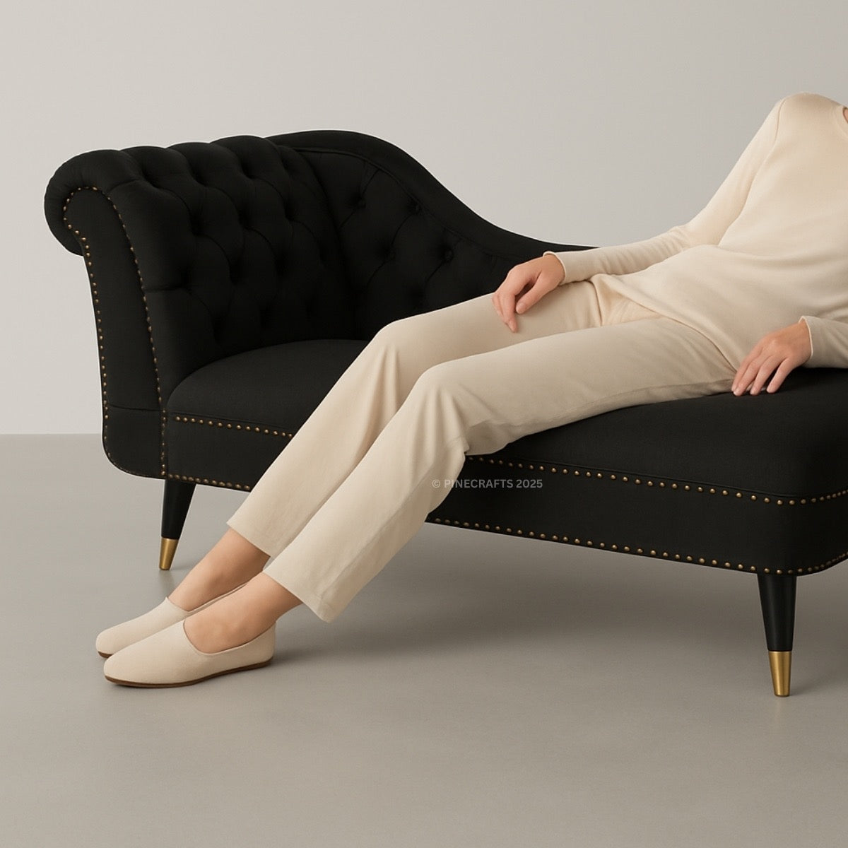 Person sitting on a black sofa with gold accents wearing beige pants and shoes.