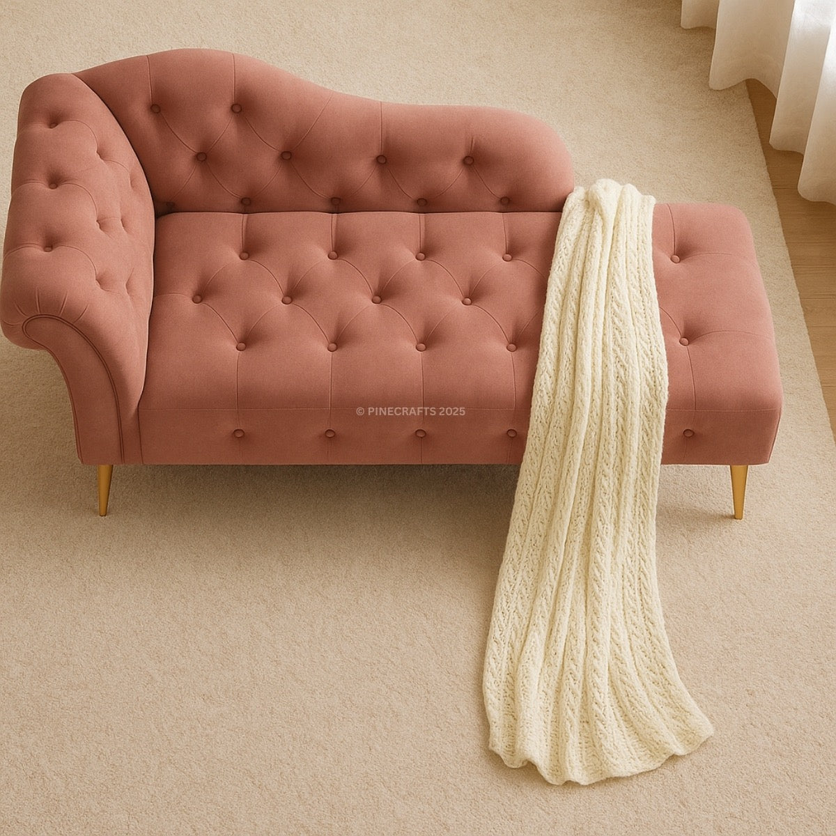 Pink tufted sofa with a white knitted blanket draped over it on a beige carpet.