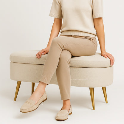 Person wearing beige pants and shoes sitting on a matching ottoman against a plain background