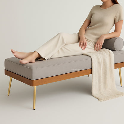 Person sitting on a modern bench with gray cushion and wooden frame, wearing a beige outfit.