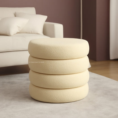Stack of beige textured cushions on a light gray rug with a blurred sofa in the background.