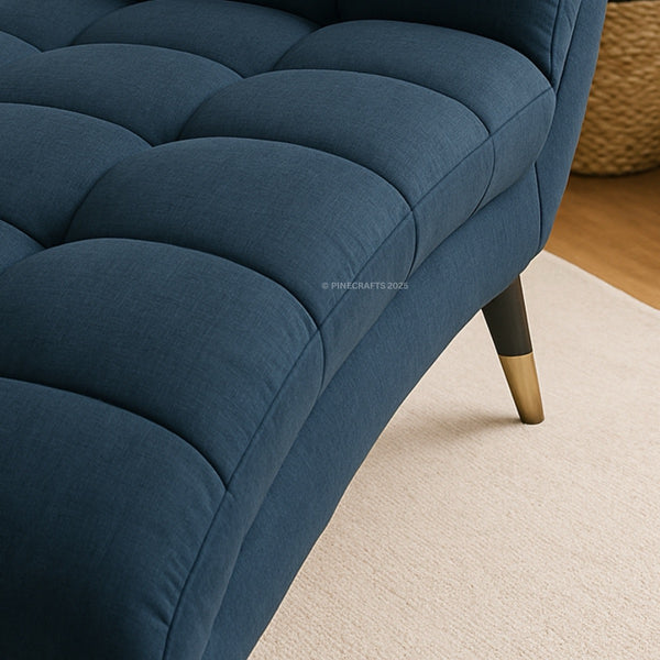 Close-up of a blue tufted sofa with gold legs on a beige carpet.