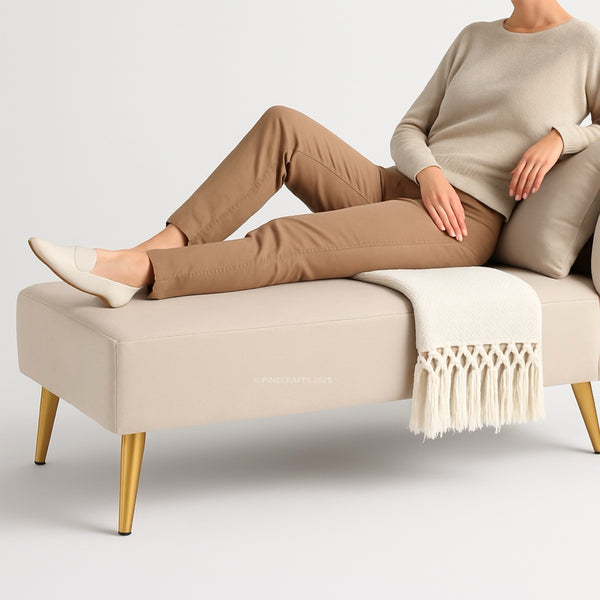 Person sitting on a beige bench with gold legs, wearing brown pants and a beige sweater.