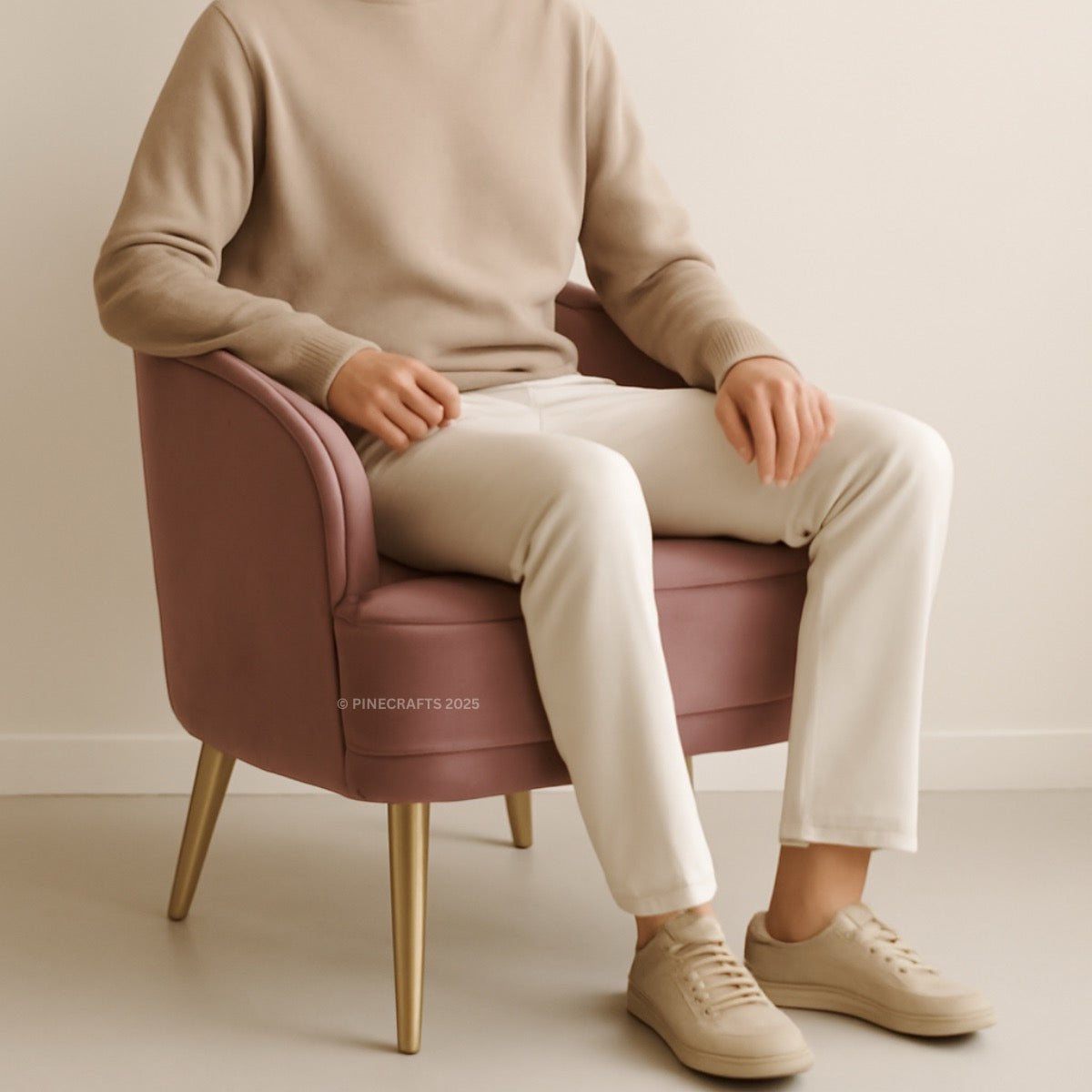 Person sitting on a pink chair wearing a beige sweater and white pants.