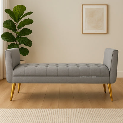 Gray tufted bench with gold legs in a room with a plant and framed picture on the wall.