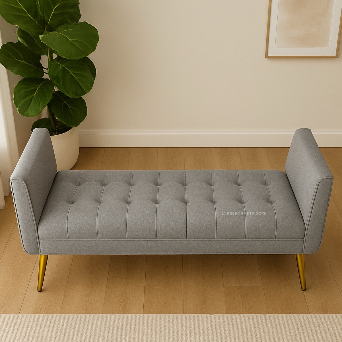 Gray tufted bench with gold legs in a room with a plant and framed picture.