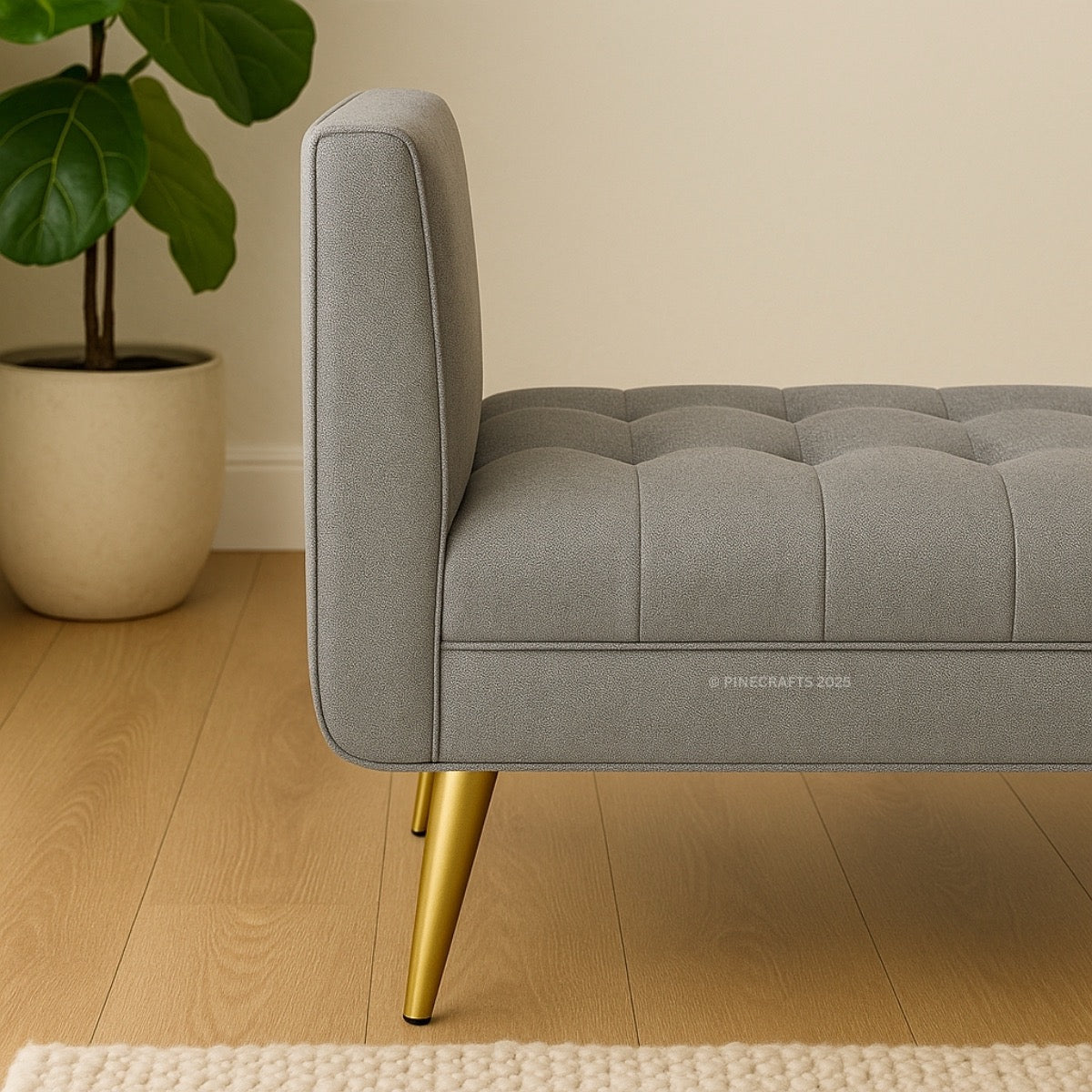 Gray tufted sofa with gold legs in a room with a plant and wooden floor.