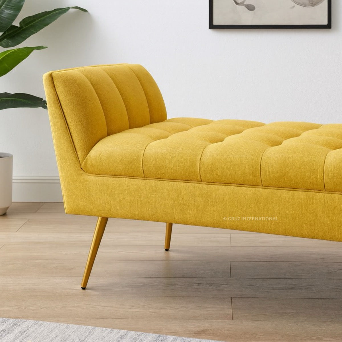 Yellow tufted bench in a room with wooden flooring and a plant.