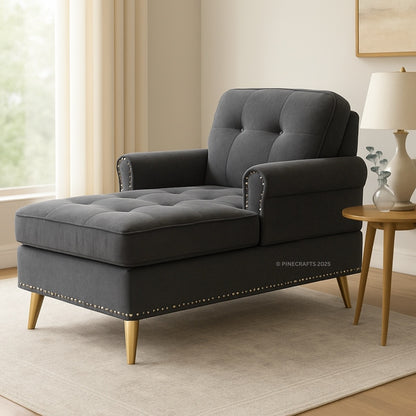 Gray tufted chaise lounge in a living room setting with a side table and lamp.