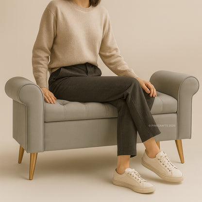 Person sitting on a gray armchair wearing a beige sweater, dark pants, and white sneakers.