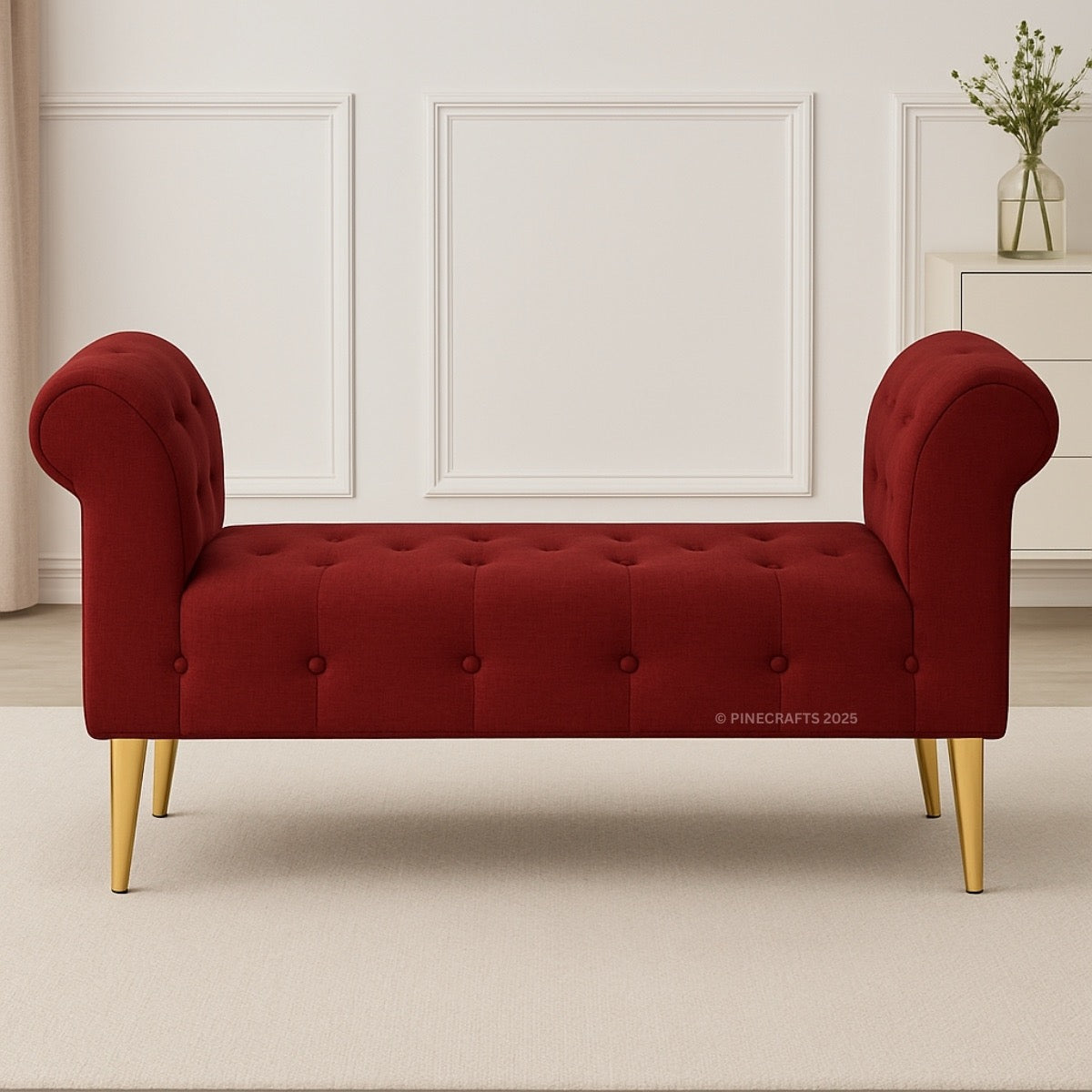 Red tufted bench with gold legs in a room with white walls and a vase.