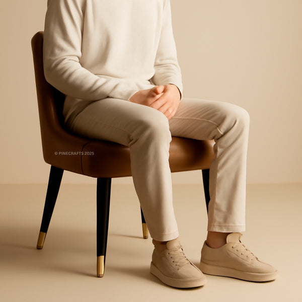 Person sitting on a brown chair wearing beige pants and shoes against a beige background