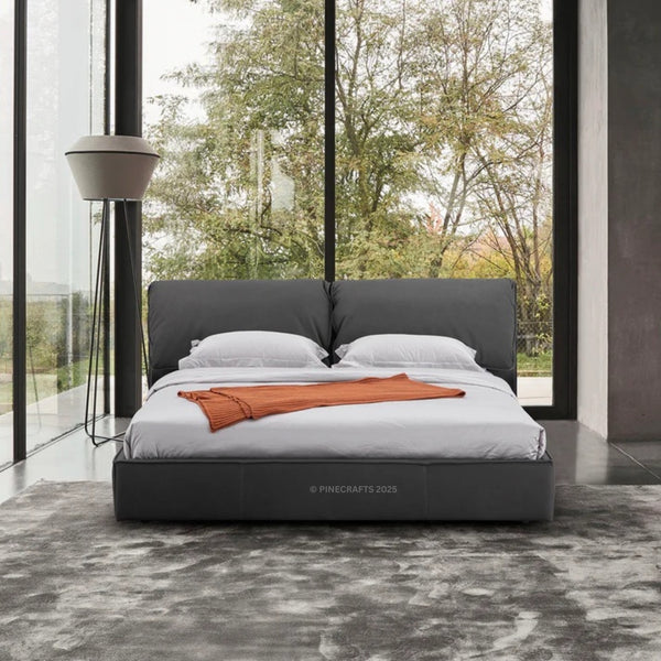 Modern bed with gray headboard and white bedding in a room with large windows.