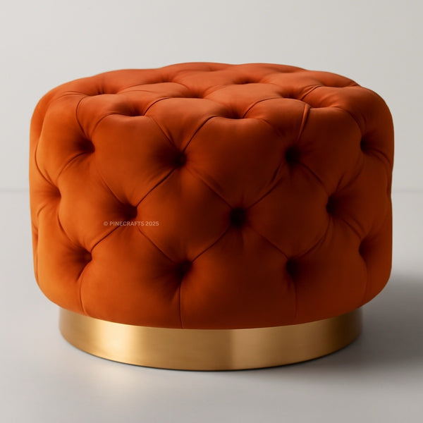 Orange tufted ottoman with a gold base on a light gray background