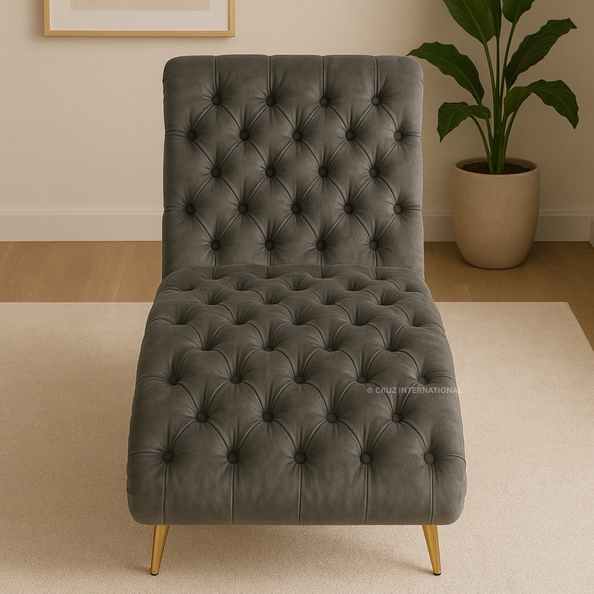 Gray tufted chair with gold legs in a room setting with a plant and framed picture.