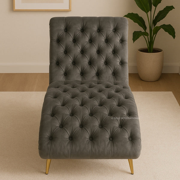 Gray tufted chair with gold legs in a room setting with a plant and framed picture.