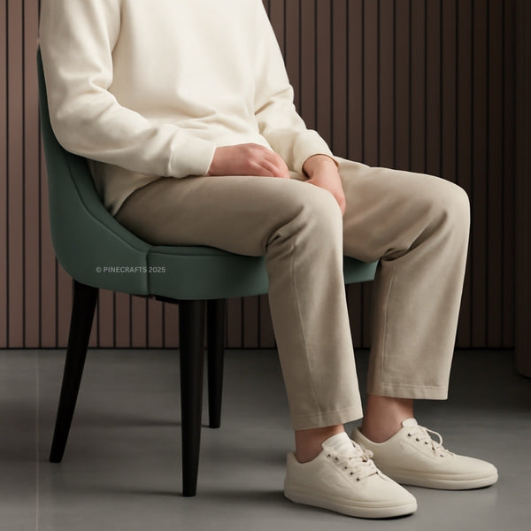 Person sitting on a green chair wearing a white sweater, beige pants, and white sneakers.
