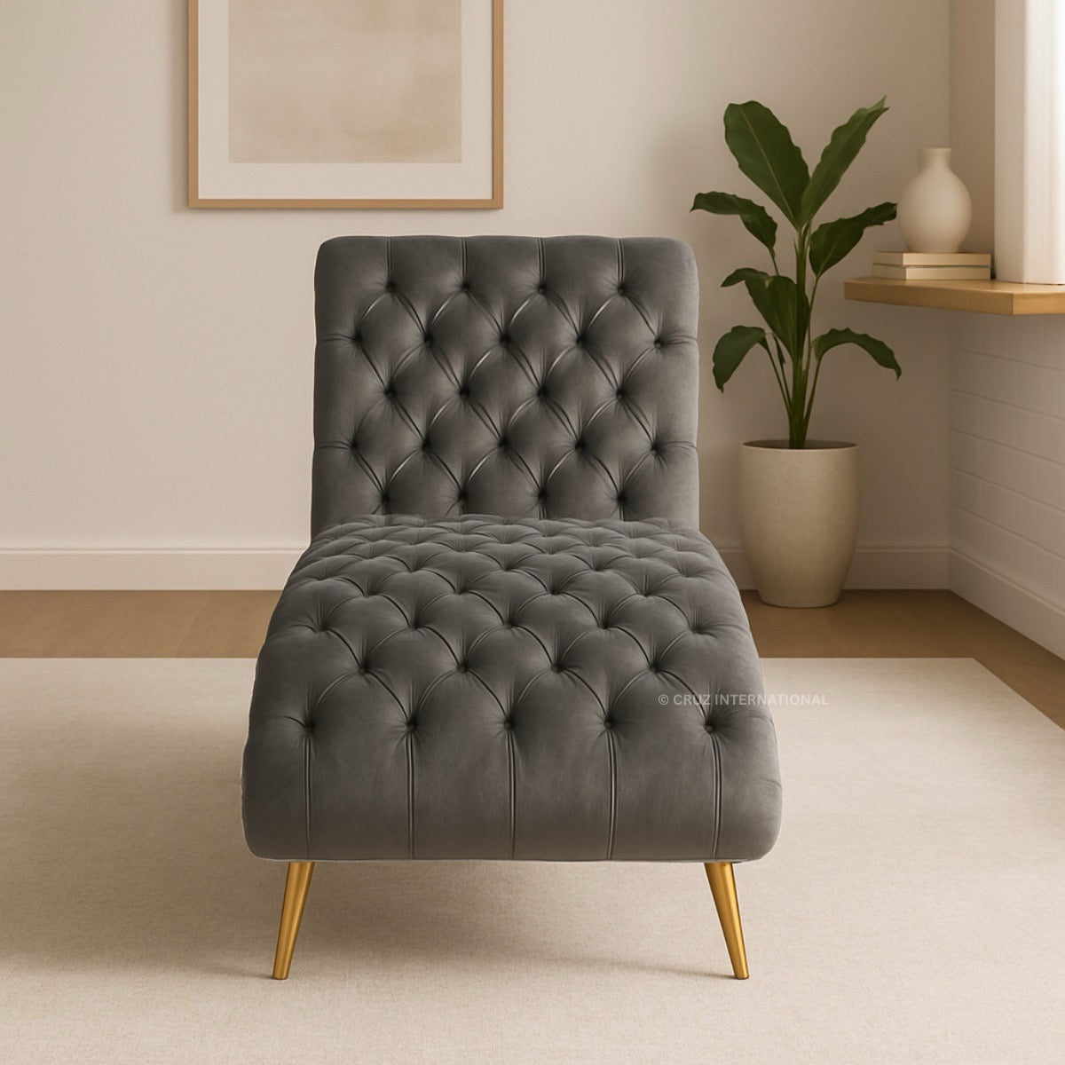 Gray tufted chaise lounge chair in a room with a plant and shelf.