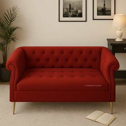 Red tufted sofa in a room with a plant, lamp, and framed pictures on the wall.
