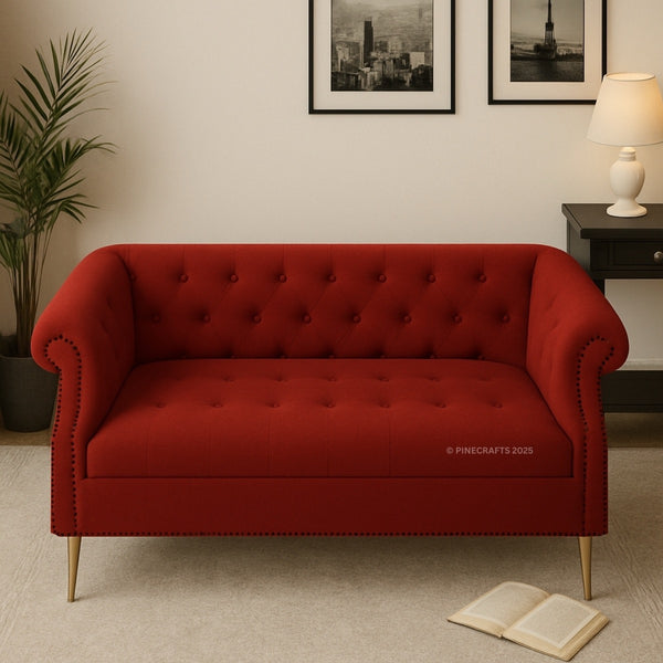 Red tufted sofa in a room with a plant, lamp, and framed pictures on the wall.