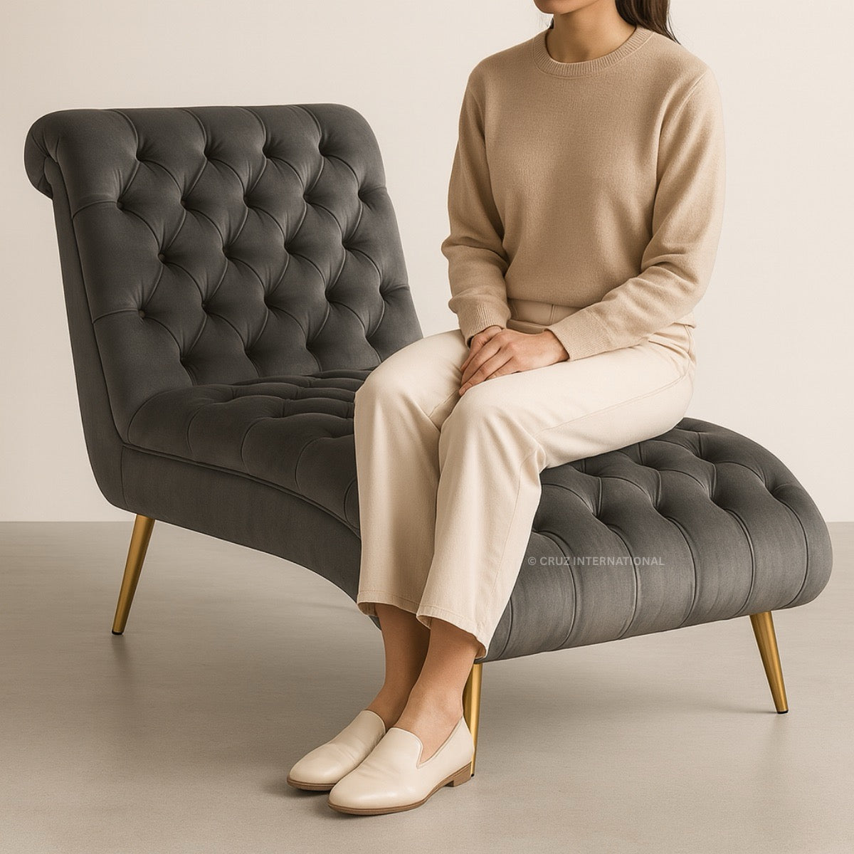 Person sitting on a gray tufted chair wearing a beige outfit.