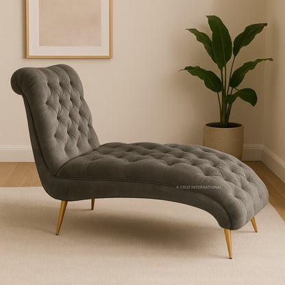 Gray tufted chaise lounge with gold legs in a room with a plant and framed picture.