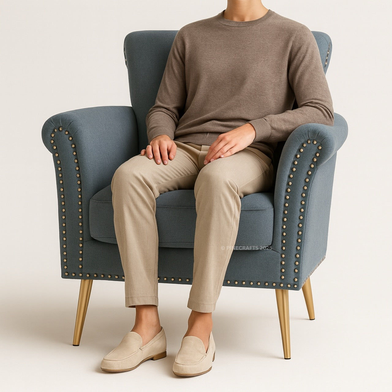 Person sitting on a blue armchair wearing a brown sweater and beige pants.