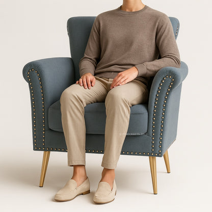 Person sitting on a blue armchair wearing a brown sweater and beige pants.