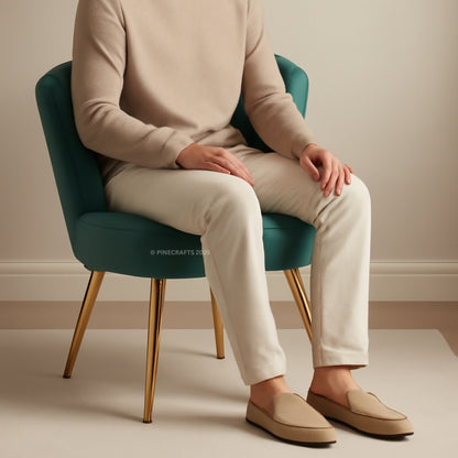 Person sitting on a teal chair wearing beige shoes, pants, and sweater.