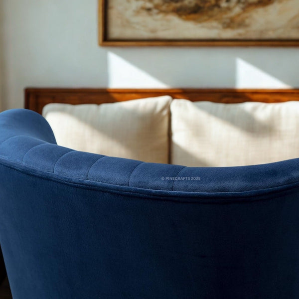 Blue velvet armchair with beige cushions in a softly lit room.