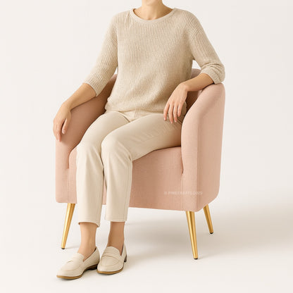 Person sitting on a pink chair wearing a beige sweater and pants with white shoes.