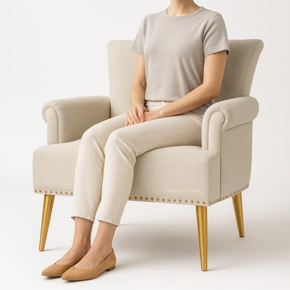 Person sitting on a beige armchair with gold legs wearing a gray shirt and beige pants.