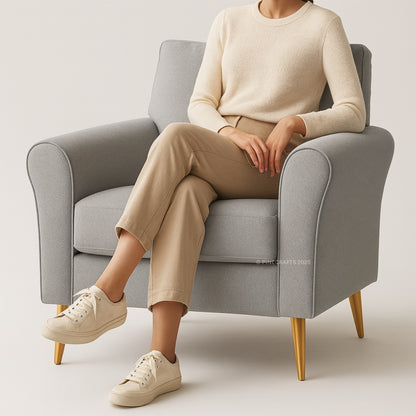 Person sitting on a gray armchair wearing a beige sweater, pants, and shoes.