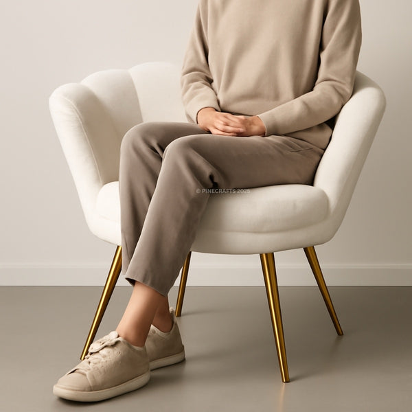 Person sitting on a white chair wearing a beige sweater and pants with matching shoes.