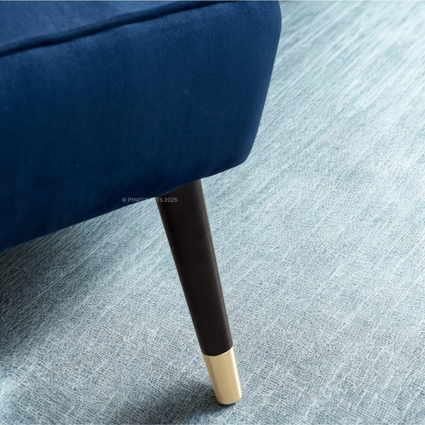 Close-up of a blue upholstered chair leg with gold tip on a gray carpet.
