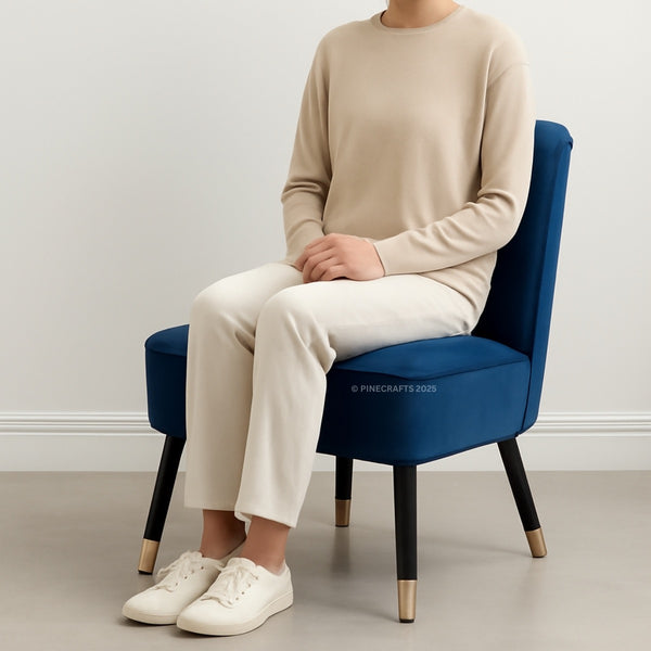 Person sitting on a blue chair wearing a beige sweater and pants with white sneakers.