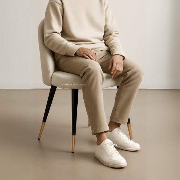 Person sitting on a chair wearing a beige sweater, beige pants, and white sneakers.